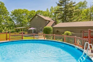 A swimming pool with a wooden deck and a house in the background.