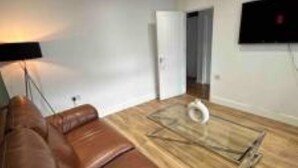 Un salon moderne avec un canapé en cuir marron, une table basse en bois et un téléviseur à écran plat fixé au mur.