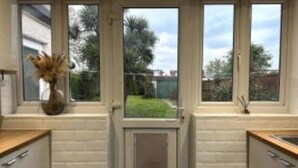 Une cuisine avec des meubles blancs, un plan de travail en bois et une fenêtre donnant sur un jardin.