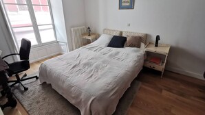 Ein Schlafzimmer mit einem großen Bett, einem Schreibtisch, einem Stuhl, einem Heizkörper und einem Fenster mit Blick nach draußen.