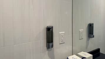 Un baño moderno con un espejo grande, dos dispensadores de toallas y una encimera negra con una caja de artículos de aseo.