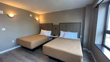 A hotel room with two single beds, a nightstand with a phone, and a window providing natural light.