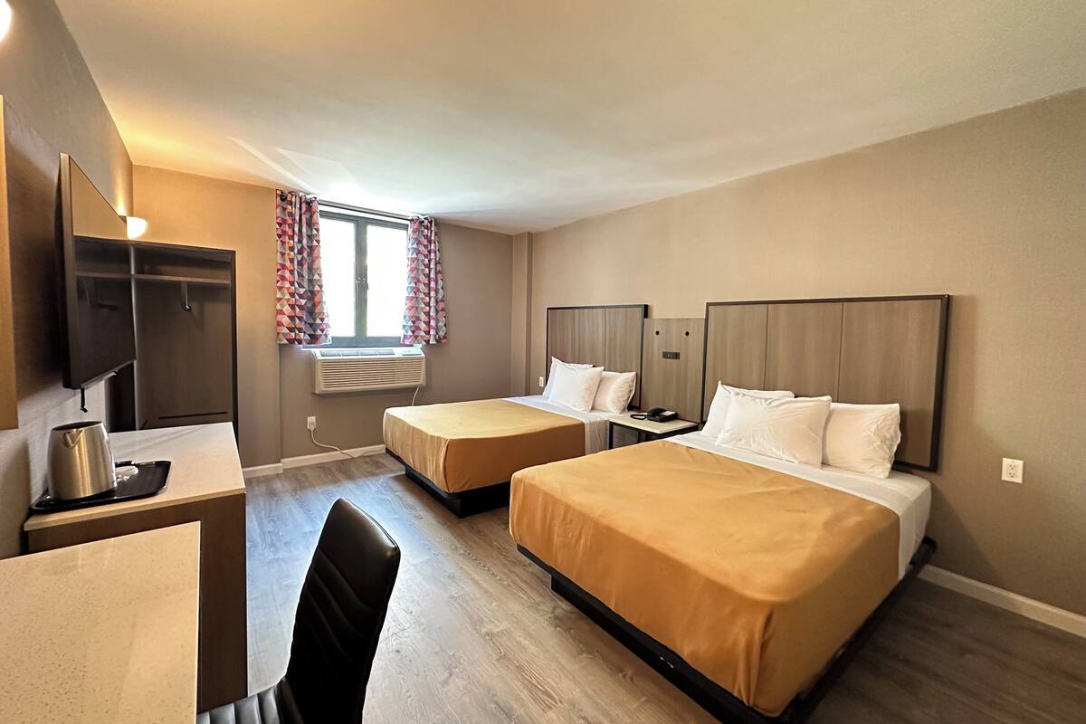 A hotel room with two beds, a desk, a chair, a TV, and a window with curtains.