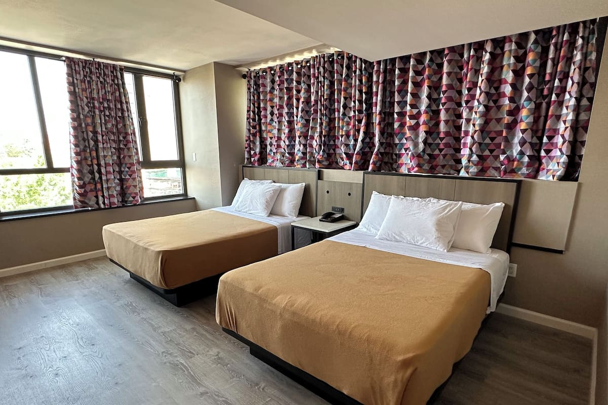 A hotel room with two beds, a small table, and a window with patterned curtains.