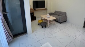 Una sala de estar moderna con un televisor de pantalla plana, un sofá gris, una mesa de centro de madera y dos taburetes.