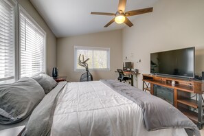 Quarto com cama, escrivaninha com computador, televisão e ventilador de teto.
