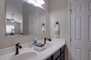 Casa de banho com duas pias, um espelho, um ventilador de teto e uma porta.