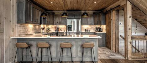 A modern kitchen with a large island, bar stools, and a wooden ceiling.