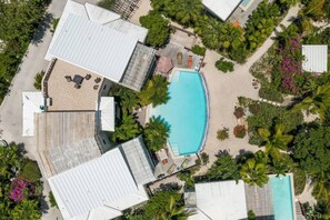 An aerial view of a resort with a central swimming pool, surrounded by lush greenery and palm trees.