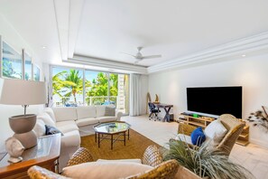 Una sala de estar moderna con sofá, mesa de centro, televisor y un balcón con vistas a palmeras.