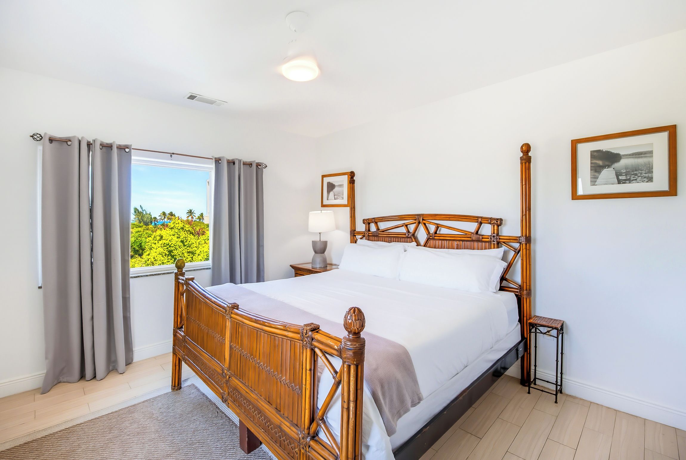 A bedroom with a wooden bed, a nightstand, a lamp, a window with curtains, and a framed picture on the wall.
