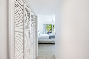 A narrow hallway leading to a bedroom with a bed, a window with curtains, and a view of greenery outside. - Stunning Yacht Club, Walk To Beach, Great Reviews! (Turtle Cove)
