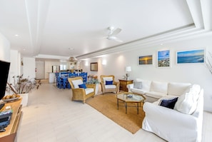 A spacious living area with a white sofa, blue chairs, a coffee table, and a dining area with blue chairs and a white table. - Stunning Yacht Club, Walk to Beach, Great Reviews! (Turtle Cove)