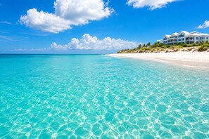 A beachfront hotel with clear turquoise water, white sandy beach, and a large building with multiple balconies.