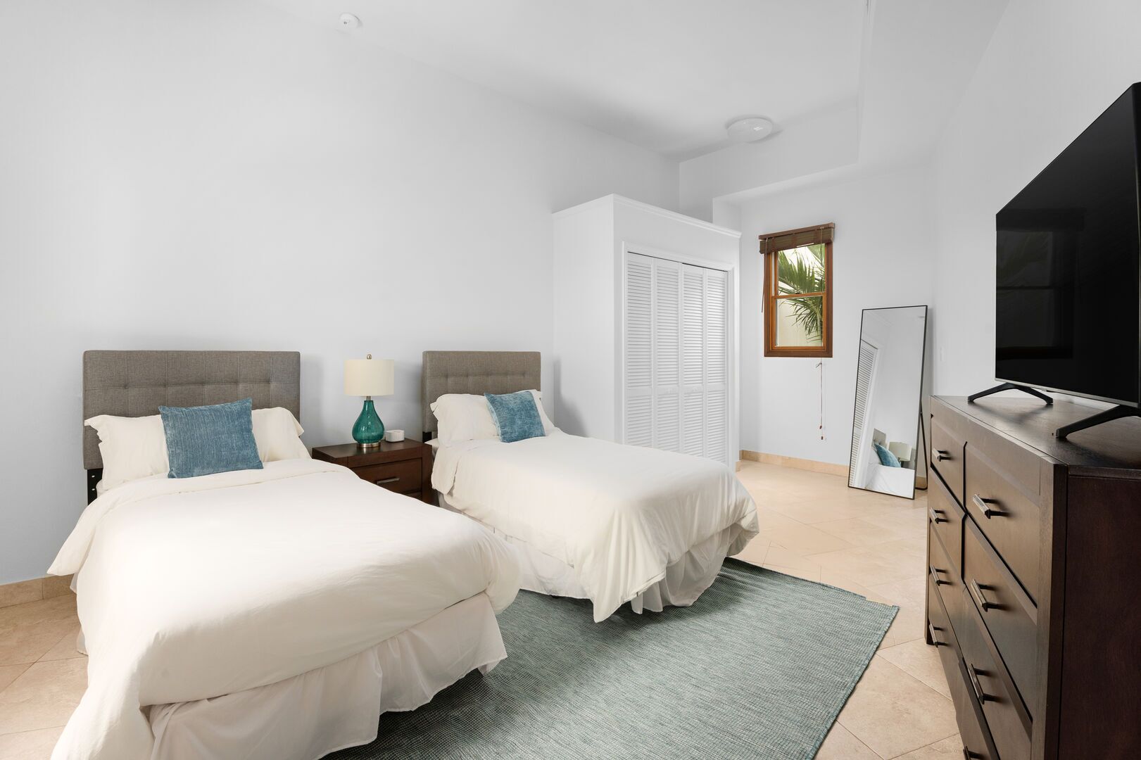 Une chambre d’hôtel avec deux lits, une télévision, une commode et une fenêtre donnant sur des palmiers.