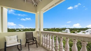 Un balcon doté d’une balustrade blanche, d’un canapé beige et d’une chaise en bois.