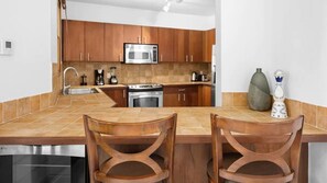 A kitchen with wooden cabinets, a microwave, a stove, and two chairs.