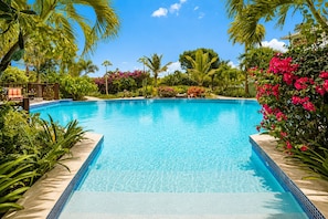 Una piscina azul cristalina rodeada de plantas tropicales y una terraza de madera.