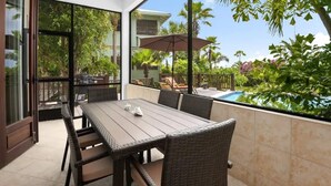 Eine Terrasse mit Tisch und Stühlen, ein Pool und üppiges Grün.