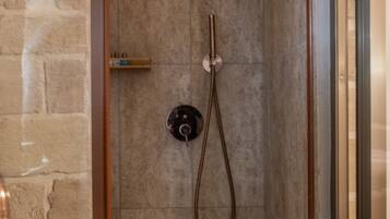 A stone-walled shower with a handheld showerhead and a control panel.