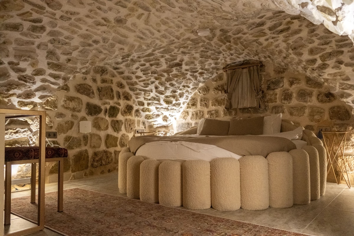 A bedroom with a stone ceiling, a large bed with a fluffy blanket, and a wooden nightstand.