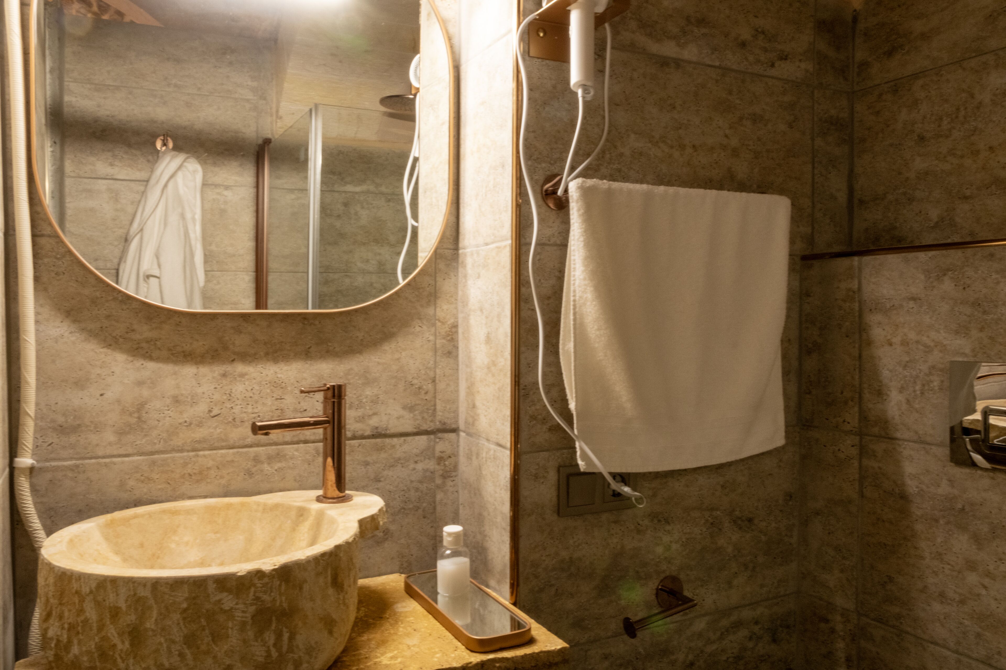 A bathroom with a round sink, a mirror, a towel rack, and a shower area.