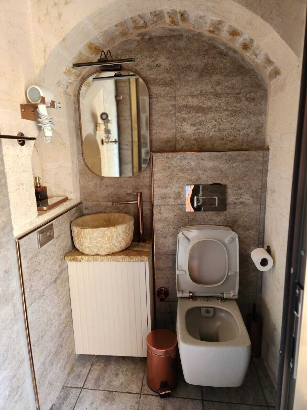Ein kleines Badezimmer mit einem Steintonne, einer Toilette und einem Spiegel.