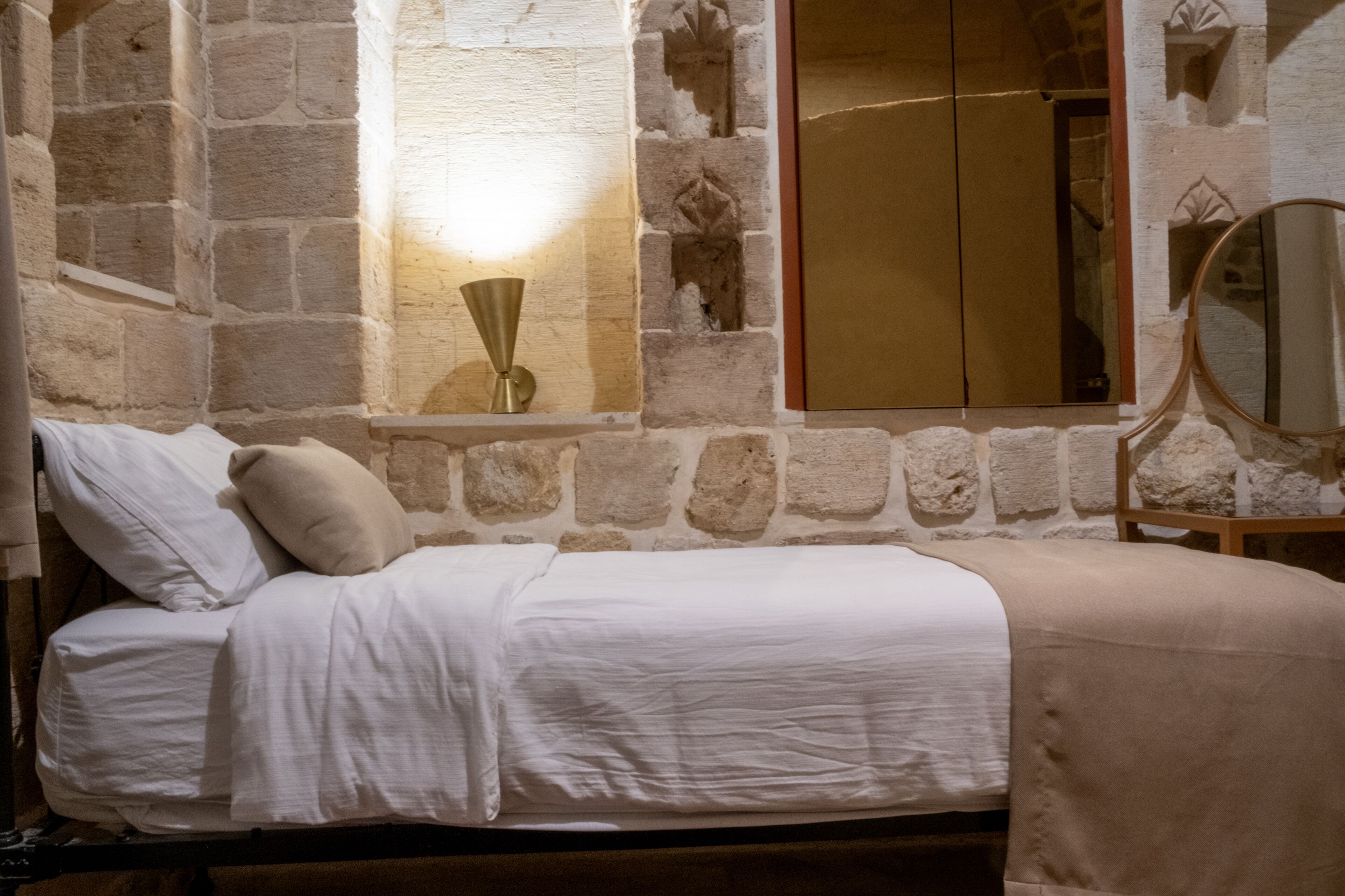 Een bed in een kamer met stenen muren, een spiegel en een wandlamp.