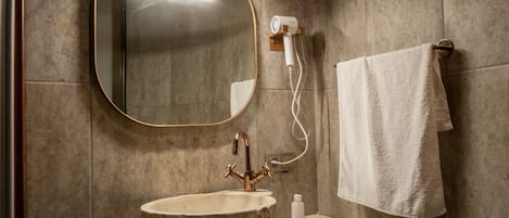 Un baño con lavabo de piedra, un espejo redondo, una toalla colgada en un perchero y un secador de pelo en la pared.