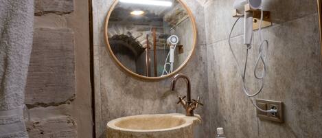 Une salle de bain avec un lavabo en pierre, un miroir rond, une douchette à main et un porte-serviettes.