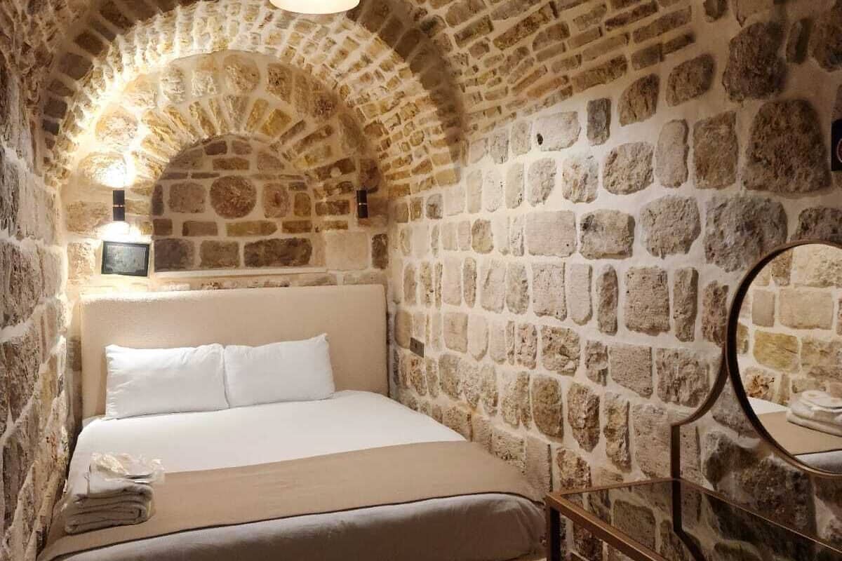 A cozy room with a stone wall, a bed, a small table, and a mirror.