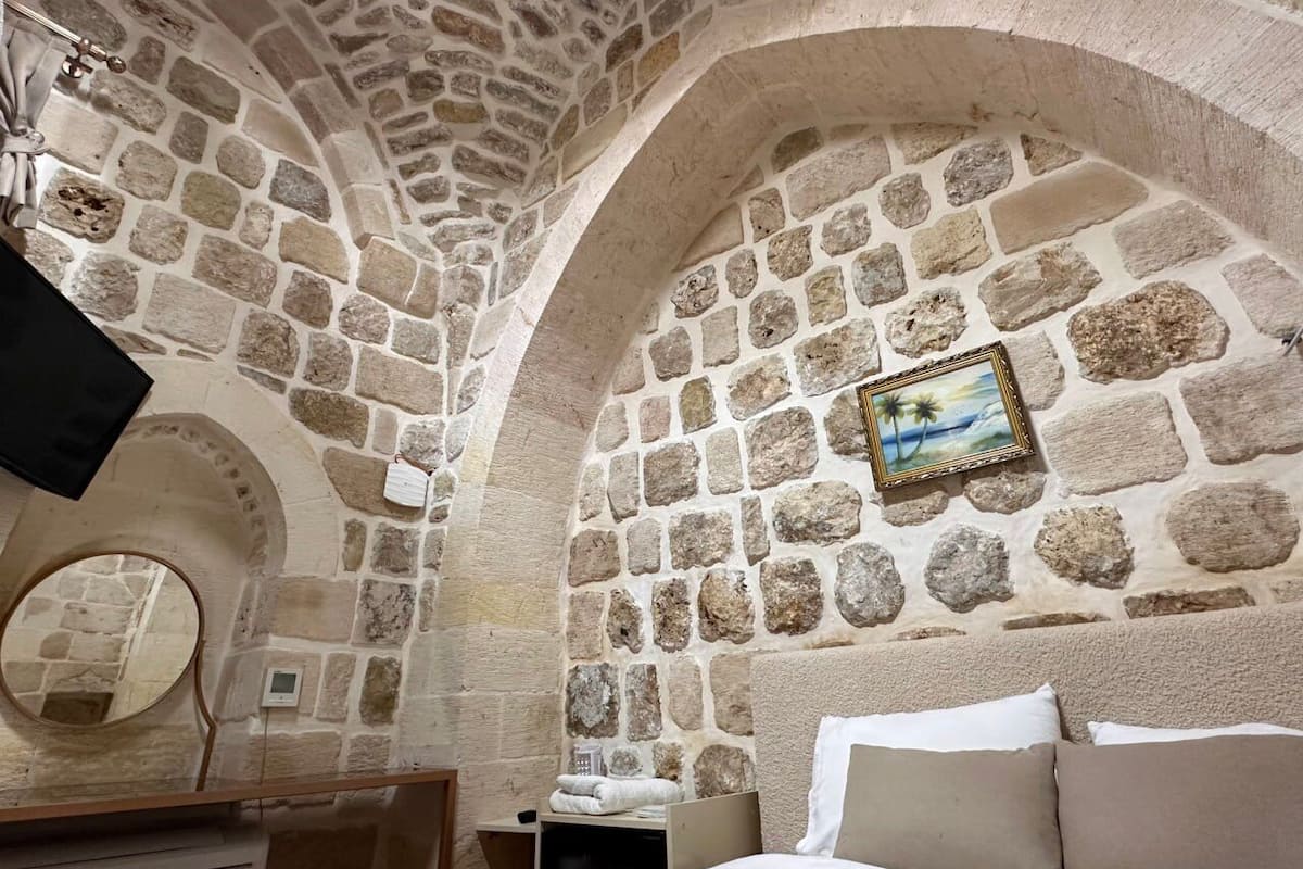 A stone-walled room with a bed, a mirror, and a picture frame on the wall.