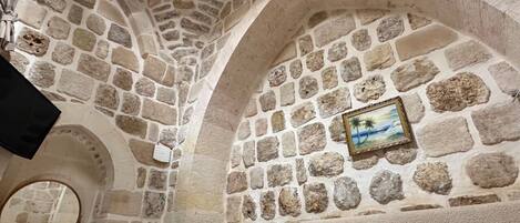 A stone-walled room with a bed, a mirror, and a picture frame on the wall.