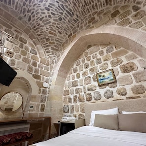 A stone-walled room with a bed, a mirror, and a picture frame on the wall. - Ana Talia House  (Mardin)