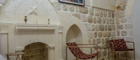 Una habitación con paredes de piedra, una chimenea, dos sillones y una mesita.