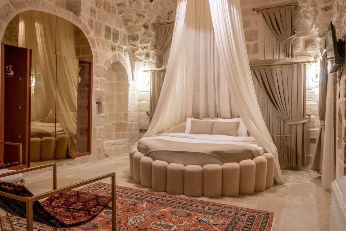 A bedroom with a round bed, a canopy, stone walls, and a large mirror.