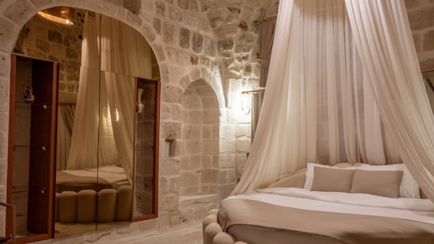 A bedroom with a stone wall, a bed with a canopy, and a mirror. - Ana Talia House (Mardin)