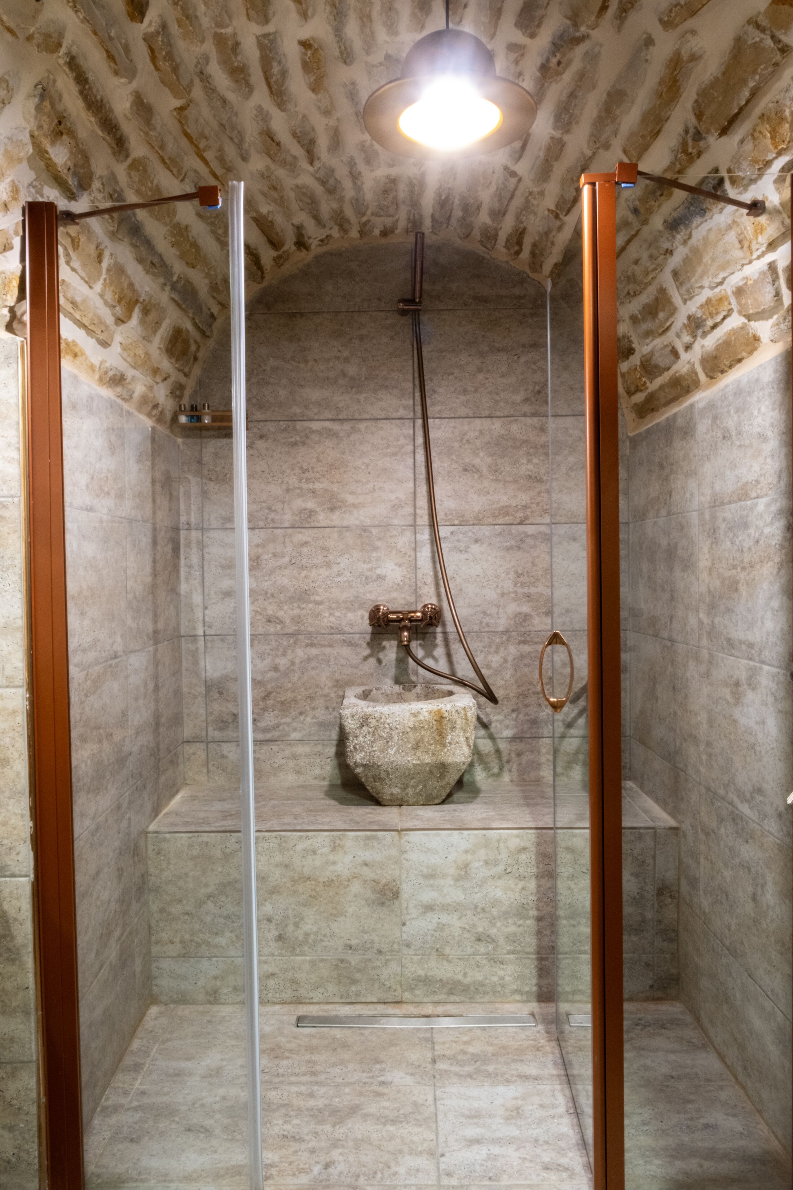 Une douche aux murs en pierre, avec un lavabo en pierre et des accessoires en cuivre.