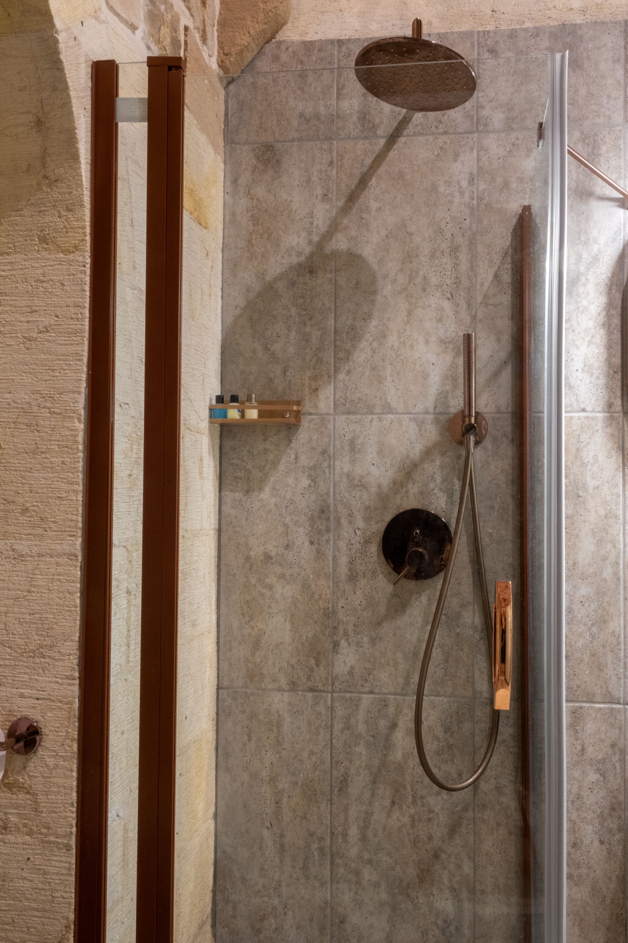 A shower area with a handheld showerhead, a wall-mounted faucet, and a drain.