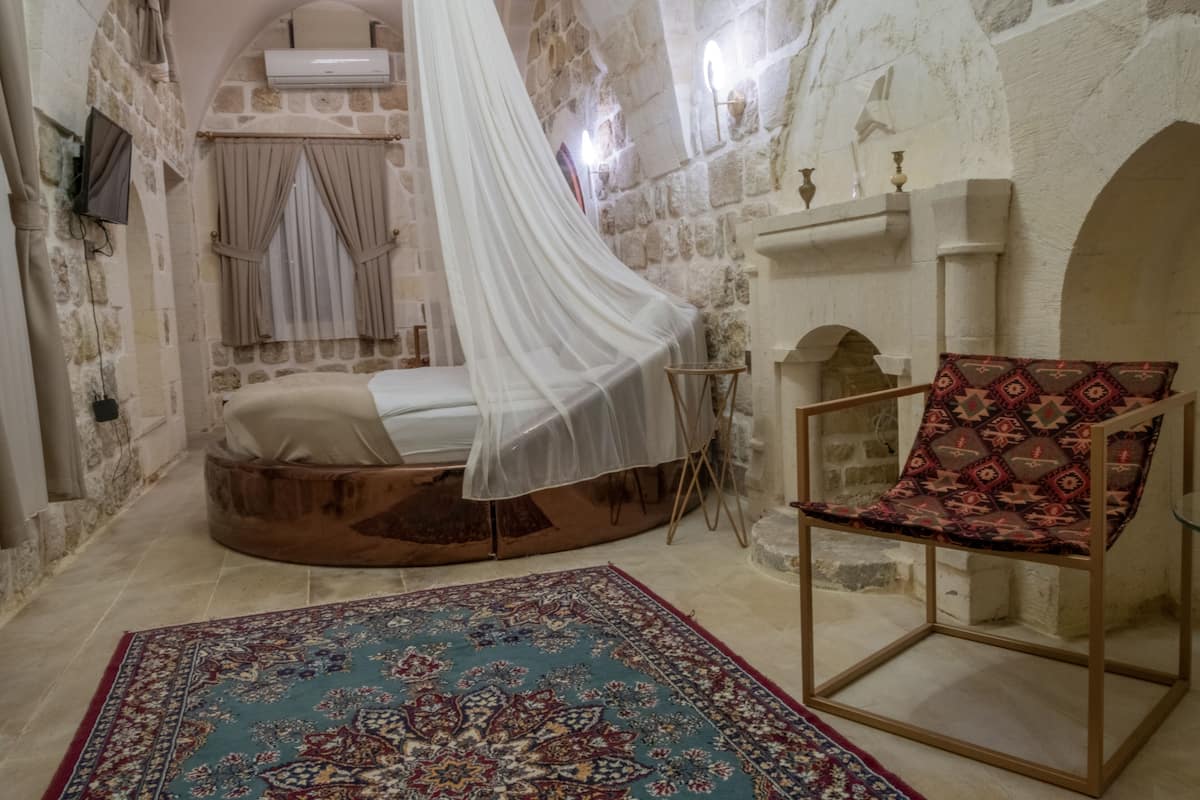 A room with a bed under a canopy, a patterned rug, and a chair with a cushion.