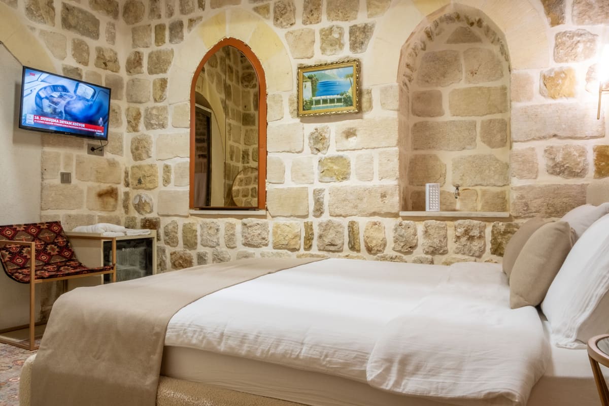 A bedroom with stone walls, a bed, a TV, and a small table with a chair.