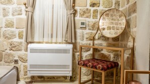 A room with a stone wall, a white air conditioner, a wooden chair with a patterned cushion, and a round mirror on the wall. - Ana Talia House (Mardin)