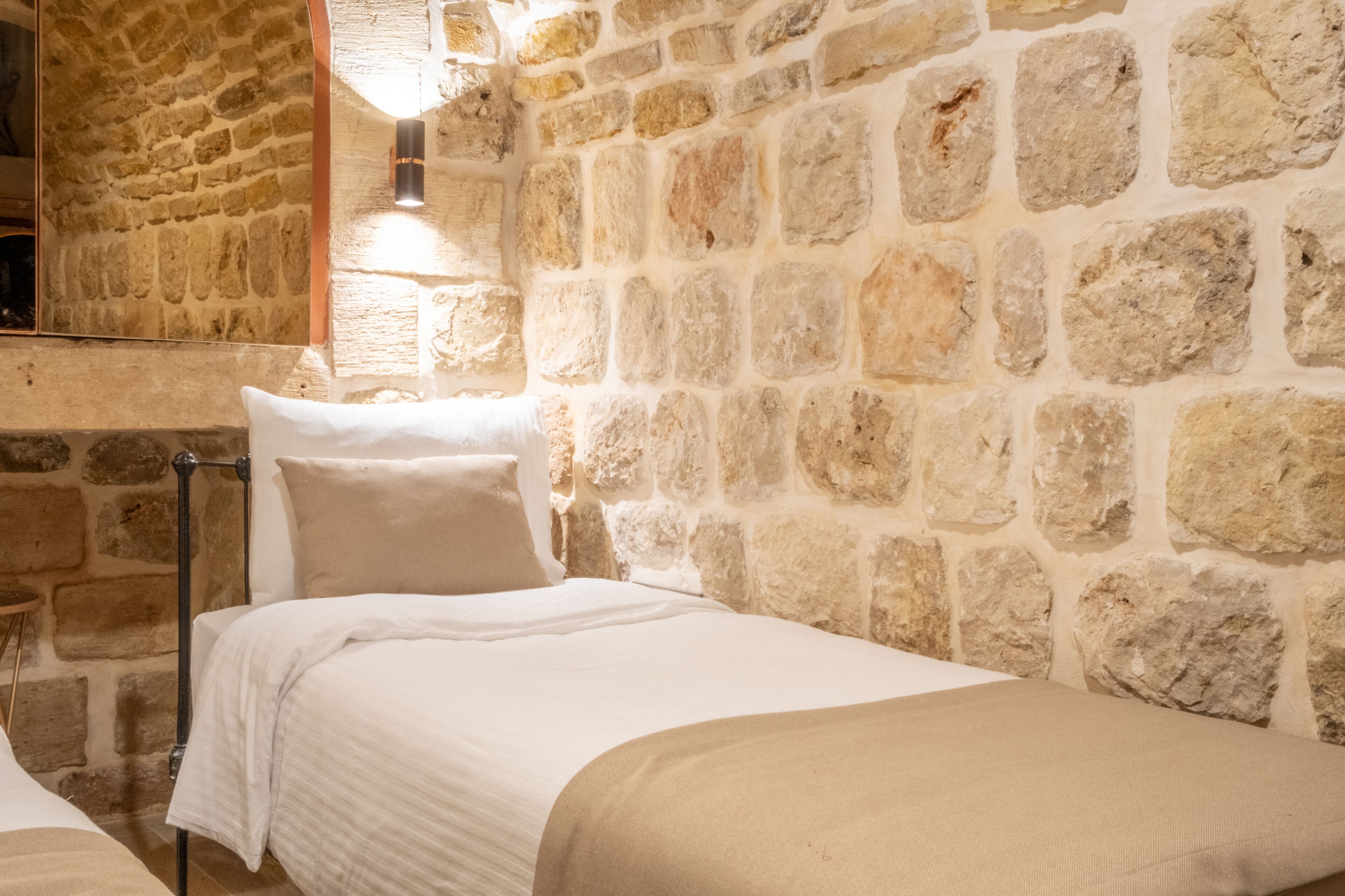 A room with a stone wall, a bed with white bedding, and a bedside table.