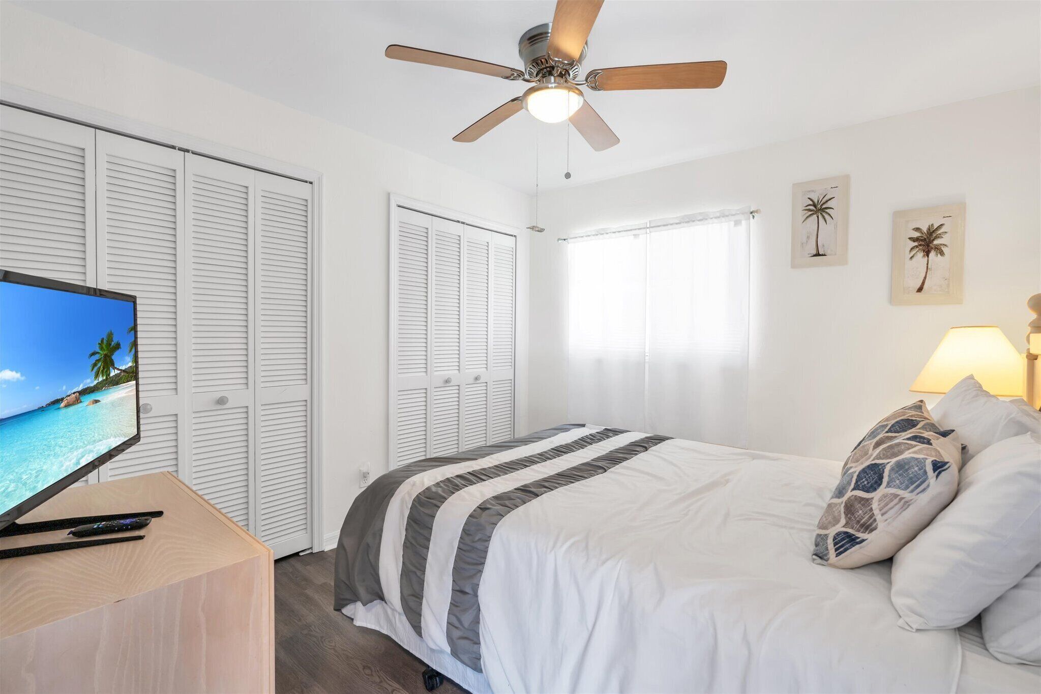 A bedroom with a bed, a ceiling fan, a TV, and a window with curtains.