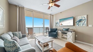 Ein modernes Wohnzimmer mit Sofa, Couchtisch und Sessel, Deckenventilator, Fernseher und Kunstwerken an der Wand.