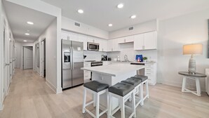 A modern kitchen with white cabinetry, a central island with bar stools, stainless steel appliances, and recessed lighting. - BEACHFRONT PROPERTY, OUTDOOR POOL, GREAT LOCATION! (Gulf Shores)