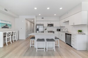 A modern kitchen with white cabinetry, a central island with bar stools, and a dining area with white chairs.