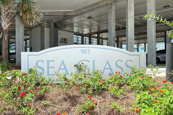 A sign for 'Sea Glass' with the number 903, surrounded by red flowers and a palm tree.