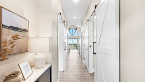 A hallway with white doors, a framed picture, a vase, and a lamp on a console table.