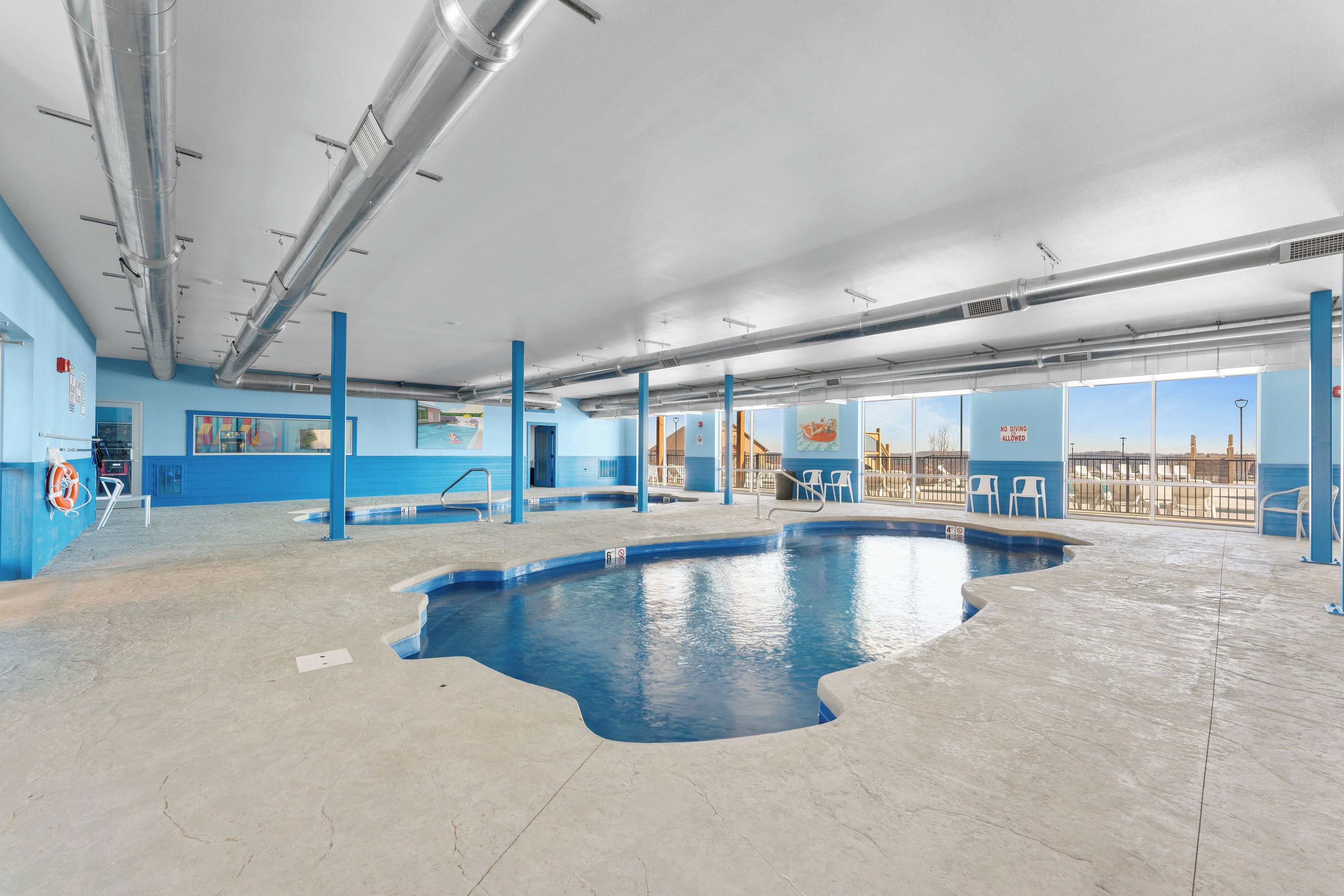 Una piscina interna con acqua cristallina e blu, circondata da pareti e colonne blu, con vista sulla città attraverso ampie finestre.